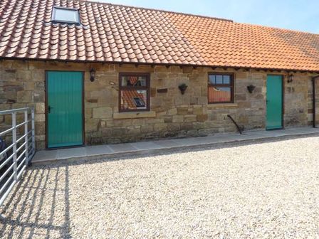 A stone building with two green doors two windows and a tiled roof at The Stable in Aislaby near Whitby