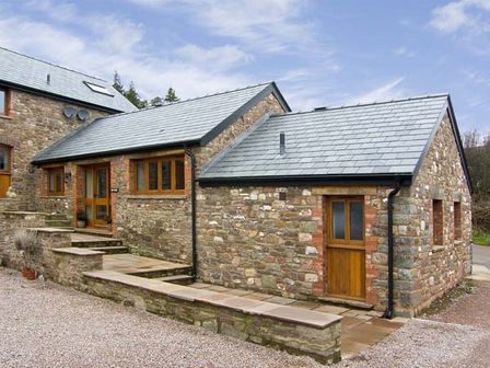 An exterior view of a stone building with slate roof and wooden doors and windows at The Byre in Llanddewi Skirrid near Abergavenny