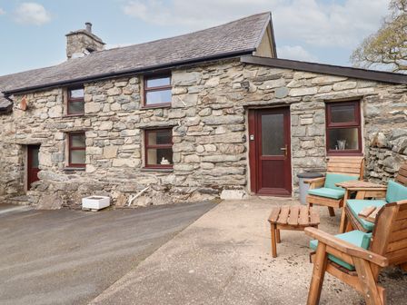 An outdoor seating area with wooden chairs and a small table outside a stone cottage at Y Bwthyn Llanbedr near Harlech