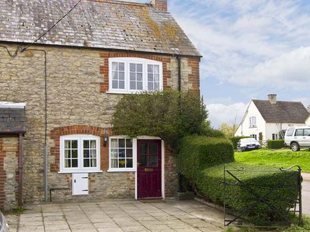 An exterior view of a stone cottage with white framed windows and a red door at Candy Cottage in Thornford near Sherborne