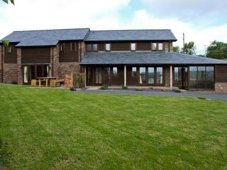 A house with brown wooden and stone walls and a large green lawn at Bushmills in Kerrys Gate near Abbey Dore
