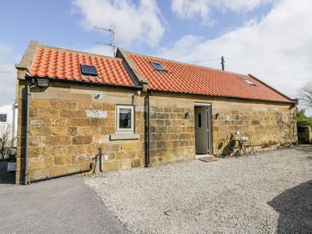 An exterior view of a stone building with a red tiled roof a small table and two chairs outside at Stable Cottage Fylingdales