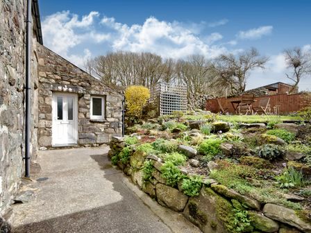 An outdoor area with a stone house entrance a stone retaining wall with plants and a patio with wooden chairs and table at Ty Capel Jeriwsalem Bronaber near Trawsfynydd