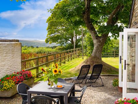 A garden patio with a table and chairs sunflowers on the table two lounge chairs large tree and a fence at Y Cartws in Newport
