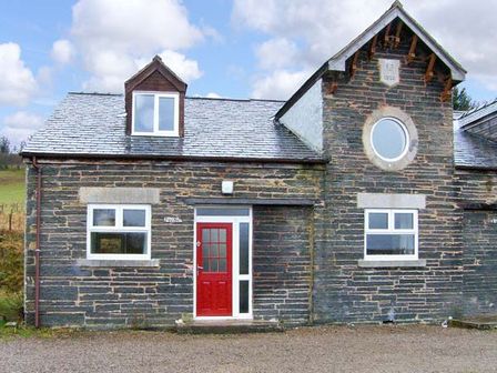 A stone house with a red door and white framed windows under a blue sky at Hendre Aled Cottage 3 in Llansannan