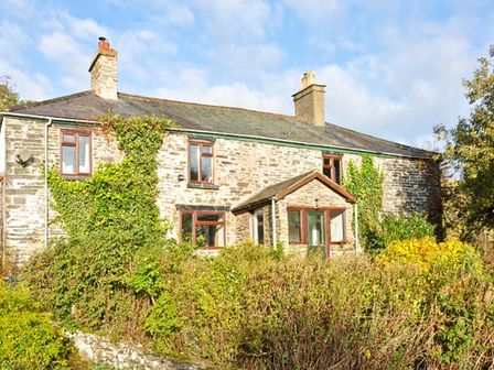 A stone farmhouse with climbing plants on the walls and a porch at Hendre Aled Farmhouse in Llansannan near Llanrwst