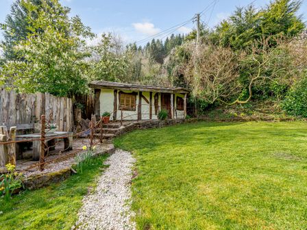 A garden with a grassy lawn a gravel path wooden bench and a small building with timber framing at Brookbank Folly in Mitcheldean