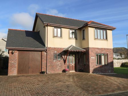 A two story house with a brick and beige exterior and a wooden front door with a driveway at Min Y Traeth in Criccieth