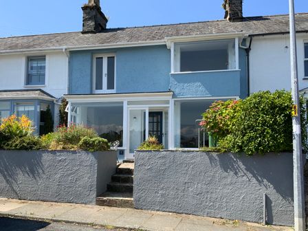 A two story blue and white terraced house with a front garden and steps leading to the door at 7 Ivy Terrace in Borth-y-Gest