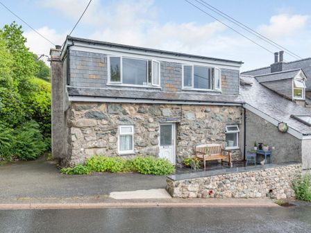 A stone house with a wooden bench and potted plants outside at Penty in Dolgellau