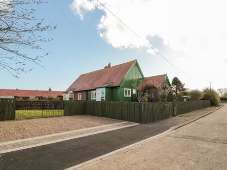 A house with a red roof and green wooden walls surrounded by a green fence and a gravel driveway at Cra-na-ge in Embleton