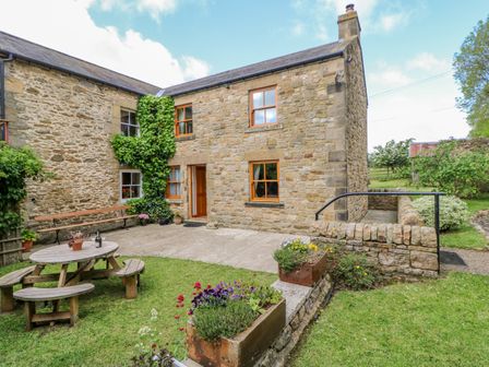 A stone cottage exterior with wooden windows a picnic table and flower planters at Moorgair Cottage in Slaley near Hexham