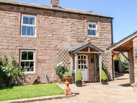 Stone house exterior with white door and windows small garden and plants near entrance at The Cow Byre in Barras near Kirkby Stephen
