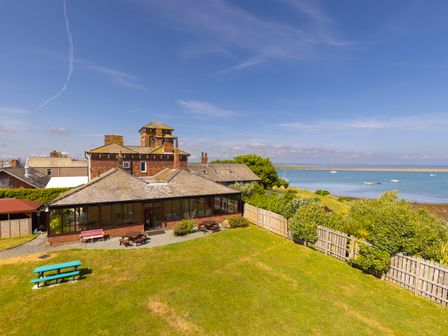 A building with a glass enclosed patio and picnic benches on a grassy area near the sea at Roa Island House in Roa Island