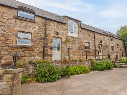 Exterior stone wall of a building with doors windows plants and a concrete pathway at Jennys Cottage in Alnmouth