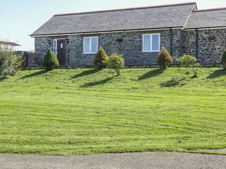 A stone house with two windows and a door with bushes in front and a grassy lawn at Middle Barn in Launceston