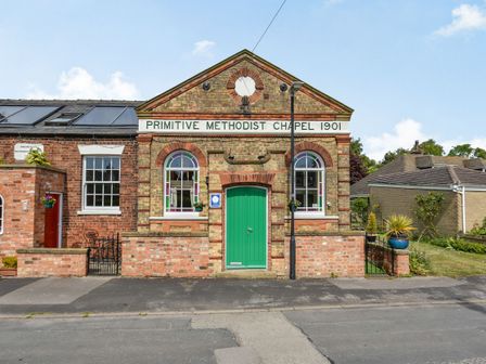 A brick building with a green door and arched windows with stained glass and a sign reading Primitive Methodist Chapel 1901 at The New Chapel in Great Hatfield near Hornsea