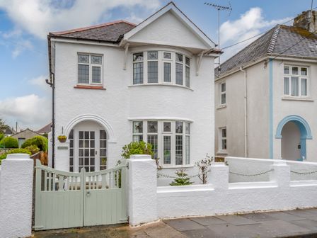 A white two-story house with a green gate and a small front garden in front of a sidewalk at Llys-y-Gan in Fishguard
