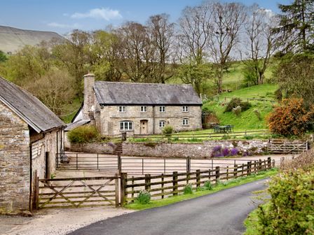 A stone house with a slate roof surrounded by fencing and greenery at The Birches in Hay-on-Wye