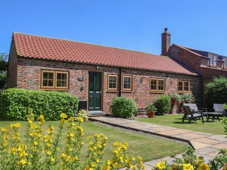 A brick cottage with a tiled roof and green door with garden furniture and flowers at Waggoner's Cottage in Bessingby near Bridlington