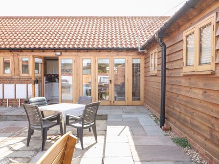 An outdoor patio with a table and four chairs in front of a building with wooden doors and windows at 5c Hideways in Hunstanton