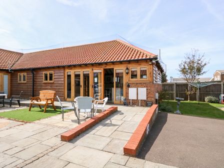 A courtyard with outdoor tables and chairs in front of a wooden building at 5d Hideways in Hunstanton