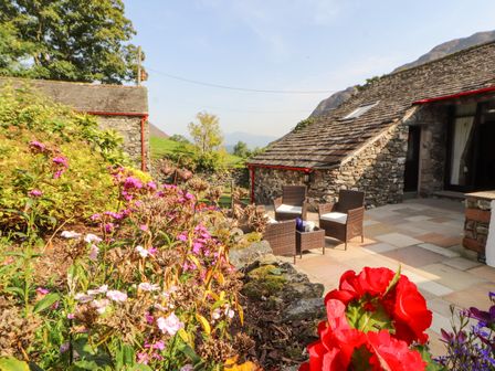 A stone patio with chairs and a table next to a stone building surrounded by flowers at The Hayloft in Newlands near Braithwaite and Keswick