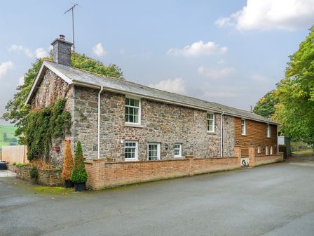 A stone and wood exterior of a long house with windows and a brick wall at Old Rectory Cottages Aberhafesp near Newtown