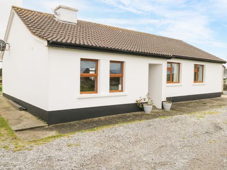 An exterior view of a single story house with white walls brown roof tiles and four windows with wooden frames at Errisbeg in Ballyconneely County Galway