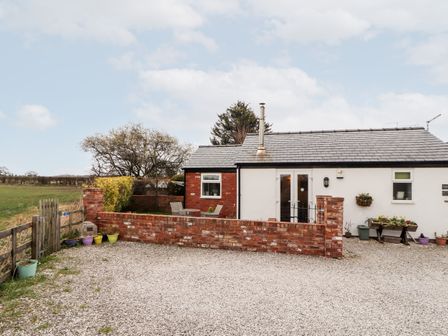 A small house with a gravel driveway a brick wall outdoor chairs and potted plants at The Old Stable in Mold