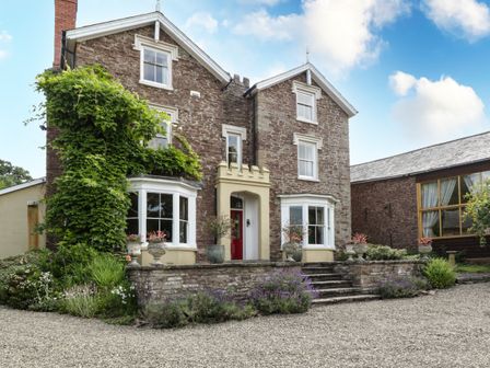 Stone house with two bay windows a red front door and potted plants at Wheelbarrow Castle in Leominster