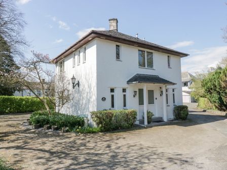 A two-story white house with a small front porch and surrounding bushes at Sandown in Bowness-on-Windermere