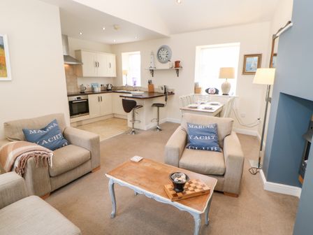 A living room with armchairs and a coffee table connected to a kitchen and dining area at Driftwood Apartment in Amble-by-the-Sea