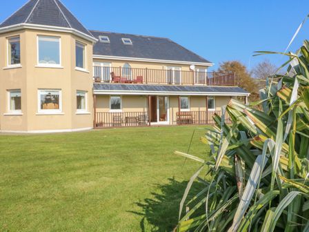 A two-story house with multiple windows and balconies overlooking a lawn with plants in the foreground at Bluebell House and Gardens in Gurteenulla near Ballydehob County Cork