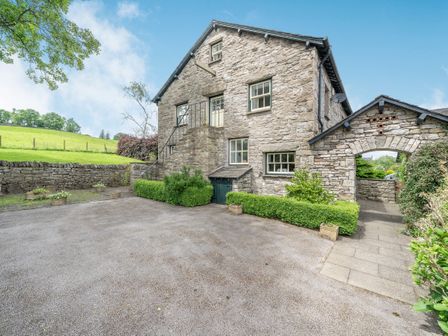 A stone building with stairs leading to a door and a stone archway with a paved pathway and greenery at 5 The Granary in Kendal