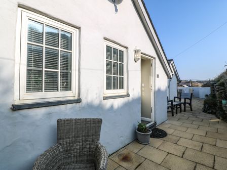 An outdoor patio area with white walls two windows a door wicker chair potted plant and seating at Tan Bryn 2 Aberdaron