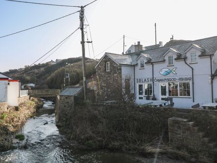 A fish bar building next to a stream with a wooden bridge and hills in the background at Tan Bryn 1 in Aberdaron