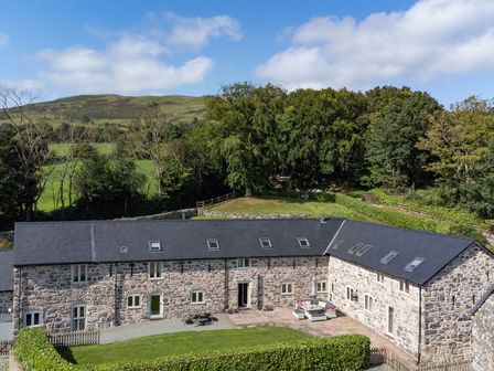 A stone building with a slate roof surrounded by green lawn and trees at Castell Courtyard in Llanrhaeadr-ym-Mochnant