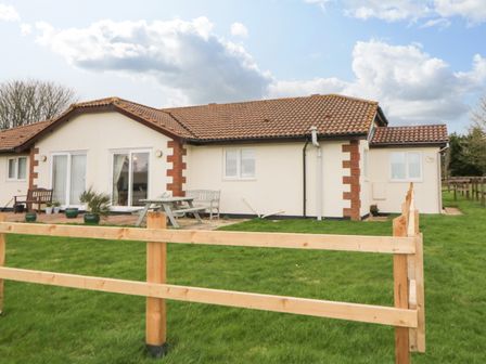 A single story house with tiled roof wooden fence and outdoor seating on grass at Broom Cottage in Stoneleigh Holiday Village near Sidmouth