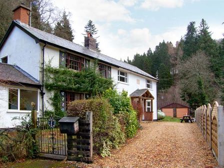 A white two story house with a gravel driveway a wooden gate bushes and trees in Forestry Cottage Rhos-y-Gwaliau near Bala