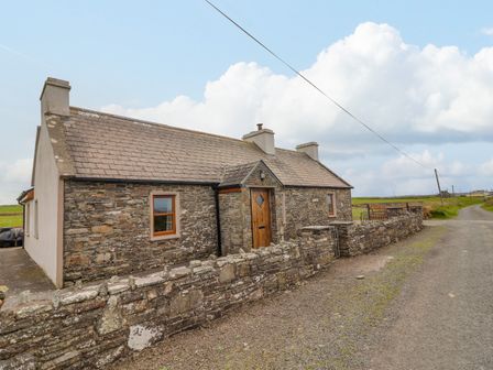 A stone cottage with a wooden door and small windows by a rural road at Clogher Cottage in Parkduff near Doonbeg County Clare