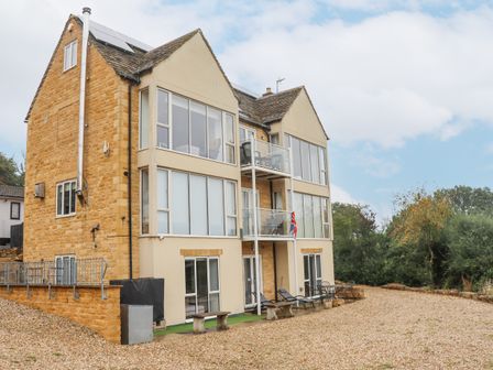 A three-story house with large windows balconies and outdoor seating on a gravel area at Beautiful Cotswold View in Bourton-On-The-Water