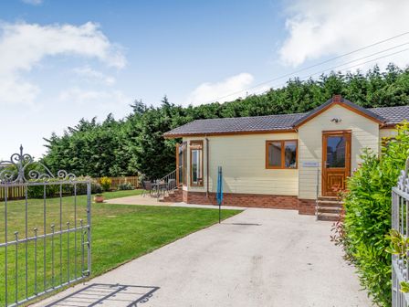 A gated driveway leading to a single-story house with a patio and garden at Elworthy Lodge in Bishops Nympton near South Molton