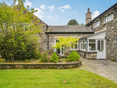A stone cottage with a small garden and trees outside at Coachmans Cottage Cartmel near Grange-over-Sands