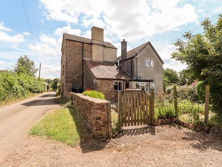 A stone and stucco house with a wooden gate and garden next to a narrow road at The Olde House in Upton Bishop