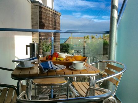 A balcony with a wooden table and metal chairs set for breakfast with fruit croissants and drinks at 4 Ocean 1 Pentire near Newquay