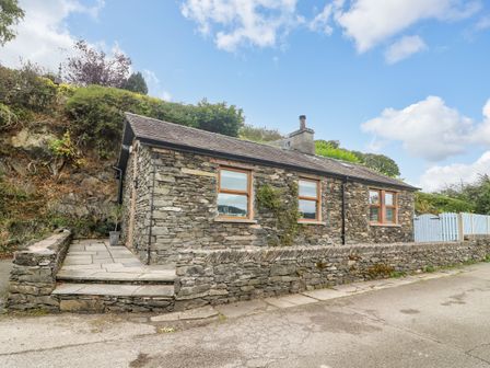A stone cottage with three windows and a stone wall along the road at The Lodge in Bouth near Newby Bridge
