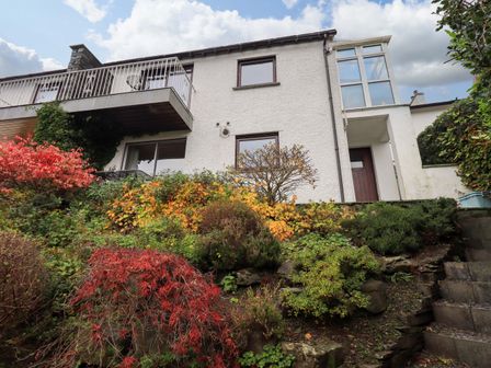 The exterior of a white two-story house with a balcony and a garden with colorful bushes and plants at Walkers Retreat in Ambleside