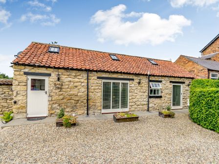 Exterior of a stone cottage with a tiled roof gravel driveway and small plants at Cow Byre Cottage in Snainton near Scarborough