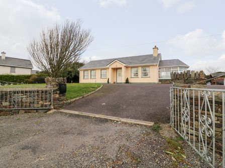 A single-story house with a driveway and a metal gate with stone walls at Raheen in Castletownshend County Cork
